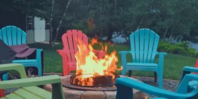 Fire burning in backyard fire pit, surrounded by blue, red, and green chairs