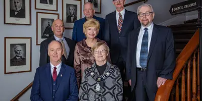 Group photo of Perth Town Council standing on staircase in front of photos of former mayors