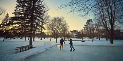 Two men skating on outdoor rink in a park at sunset