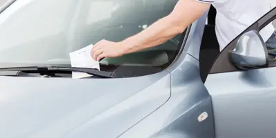 Person taking a parking ticket off of car windshield