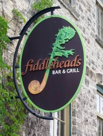 Round sign protruding out of stone building that says Fiddleheads Bar & Grill