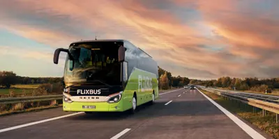 Green bus driving down highway during sunset